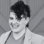 A black and white photo of a light-skinned nonbinary person with a curly mohawk